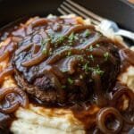 Hamburger Steak with Onion Gravy (Classic, Juicy & Comforting) Juicy hamburger steak with onion gravy served over mashed potatoes in a skillet