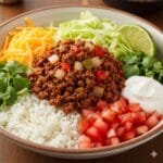 Family-friendly taco rice bowl with rice, seasoned ground meat, beans, corn, lettuce, cheese, and salsa.