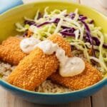 Crispy breaded fish served over rice with fresh cabbage slaw and creamy chipotle sauce in a colorful dinner bowl