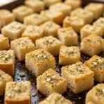 Homemade garlic croutons baked until golden and crispy on a sheet pan, made with crusty bread, olive oil, butter, and herbs