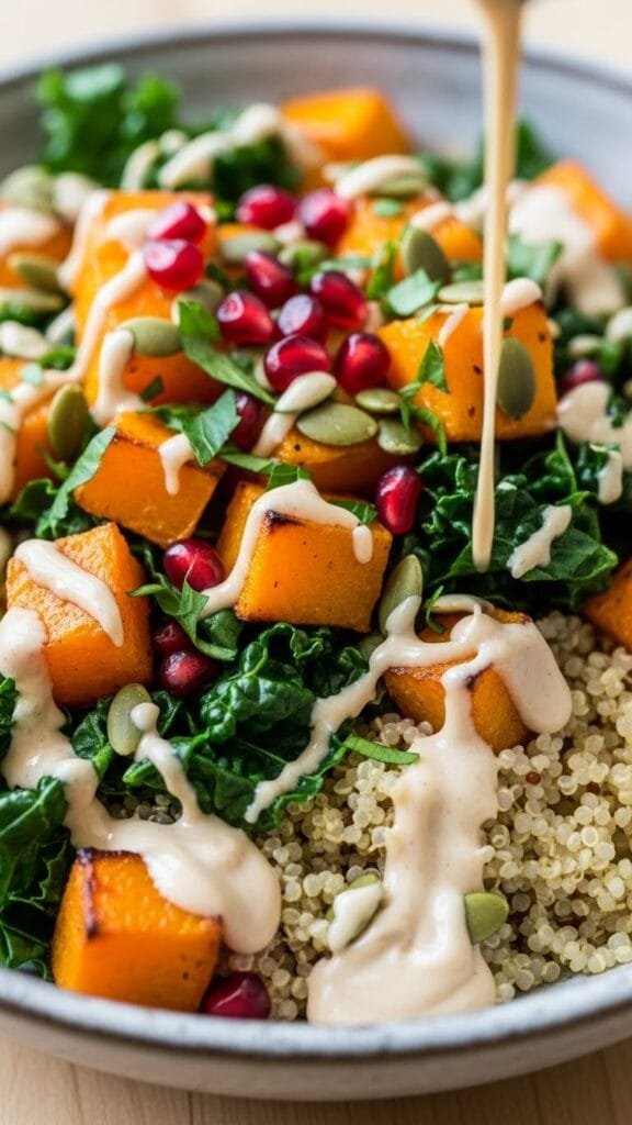Maple-roasted butternut squash quinoa bowl topped with greens, nuts, and creamy tahini dressing