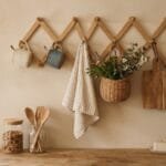 Wooden accordion peg rack styled with mugs, a linen towel, wicker basket, dried greenery, and a cutting board in a cozy farmhouse kitchen.