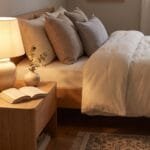 Cozy bedroom with a glowing ceramic bedside table lamp, neutral bedding, natural wood furniture, and warm decorative details.