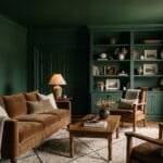 Moody color-drenched living room with deep green walls, matching trim, warm lighting, textured furnishings, and natural wood decor.