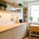 Small apartment kitchen with smart storage, open shelves, compact dining table, warm lighting, and indoor plants.